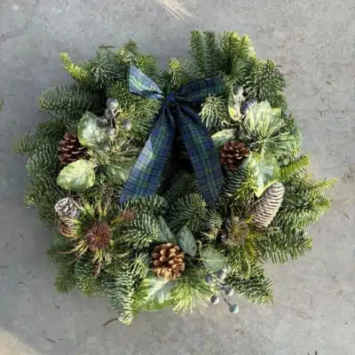Highlander Christmas wreath with navy and green tartan bow, pine cones and thistles